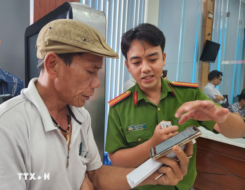 Cán bộ công an hướng dẫn người dân thao tác xin cấp phiếu lý lịch tư pháp trên ứng dụng VNeID. (Ảnh: TTXVN)